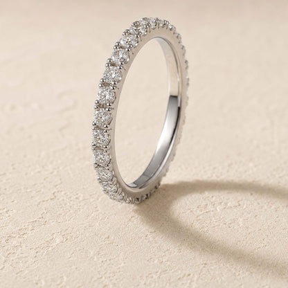 Sterling silver moissanite eternity ring standing on cream surface, micro-pavé band detail visible