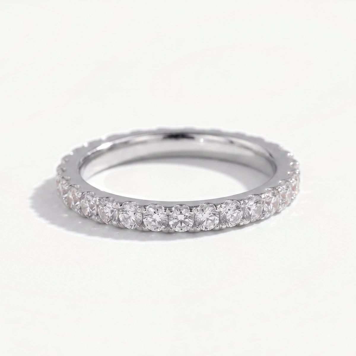 Sterling silver moissanite eternity ring leaning on a near white ground, full pavé of claw set stones