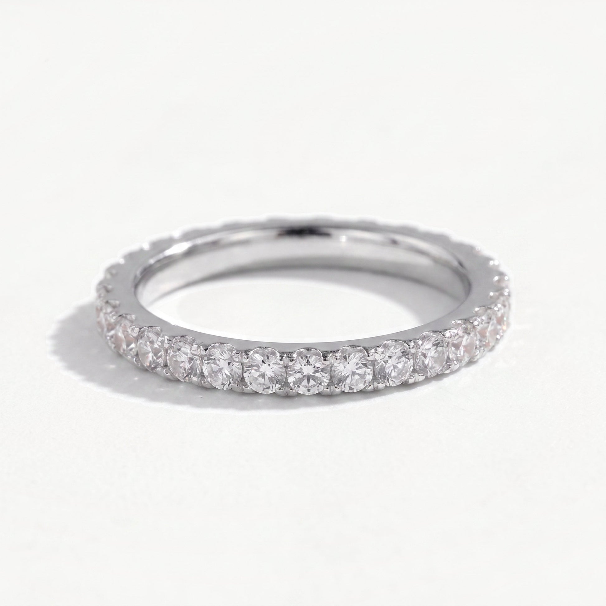 Sterling silver moissanite eternity ring leaning on a near white ground, full pavé of claw set stones