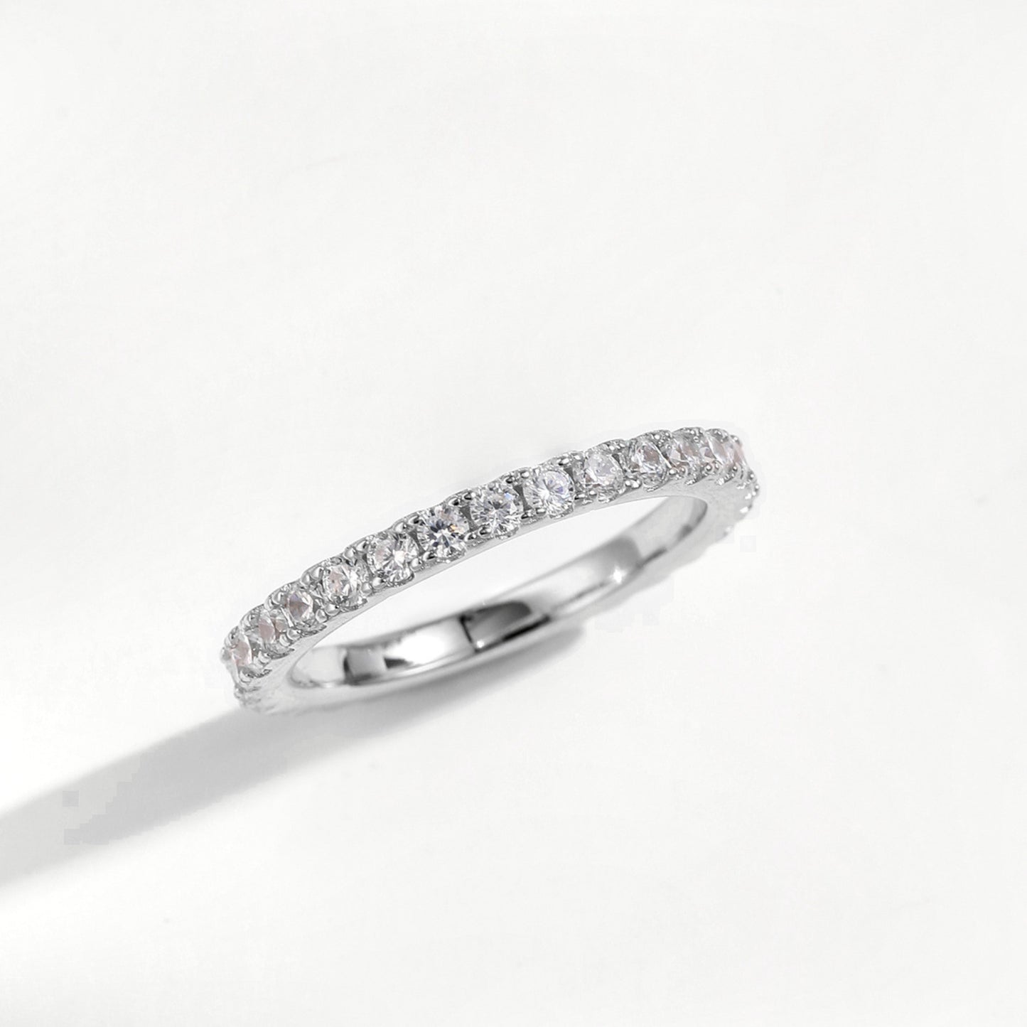 Slim 2 mm sterling silver moissanite eternity ring lying flat, claw set round stones along the band