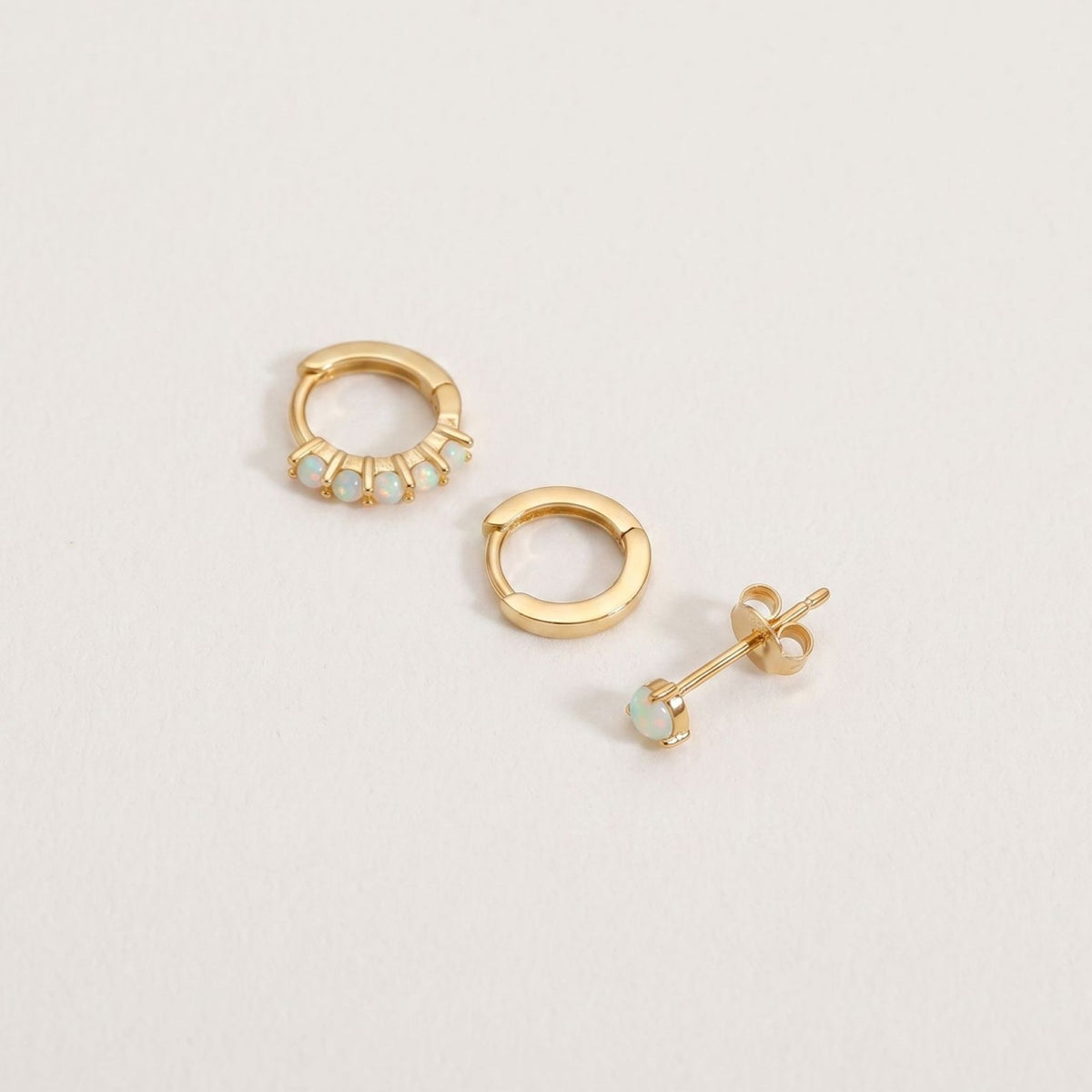 Gold plated opal earring set of three on a plain near-white background, huggie hoop, plain hoop and stud