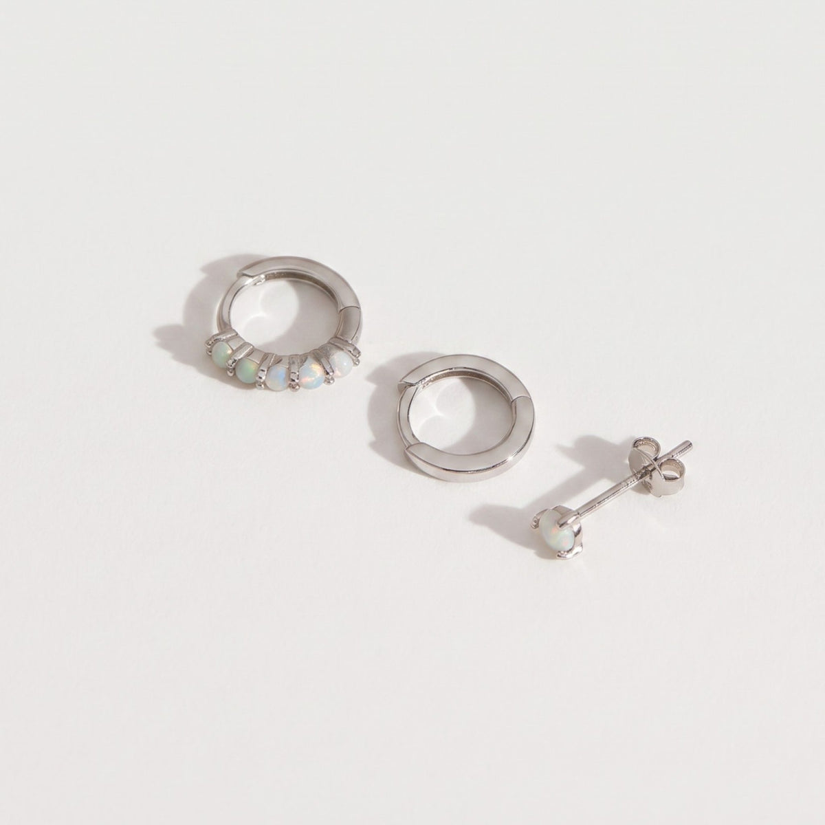Sterling silver opal earring set of three on a plain near-white background, huggie hoop, plain hoop and stud