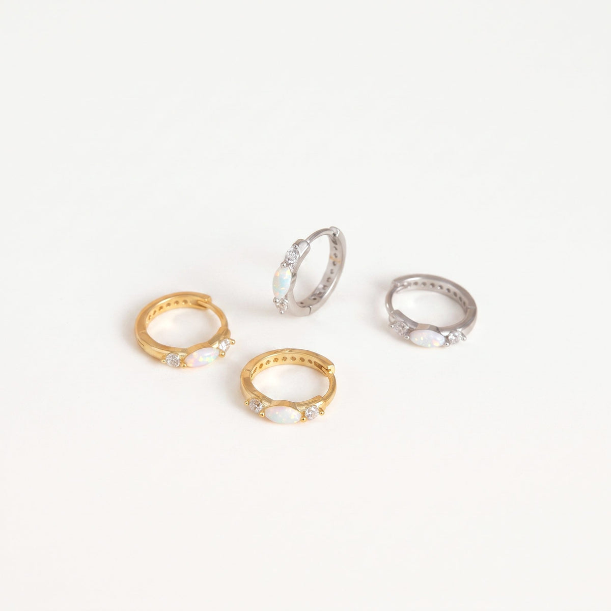 Gold and white gold opal huggie hoop earrings with cubic zirconia accents on a plain near-white background