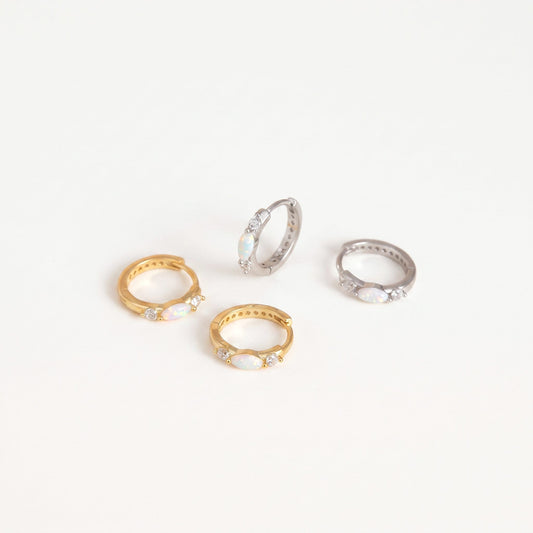 Gold and white gold opal huggie hoop earrings with cubic zirconia accents on a plain near-white background