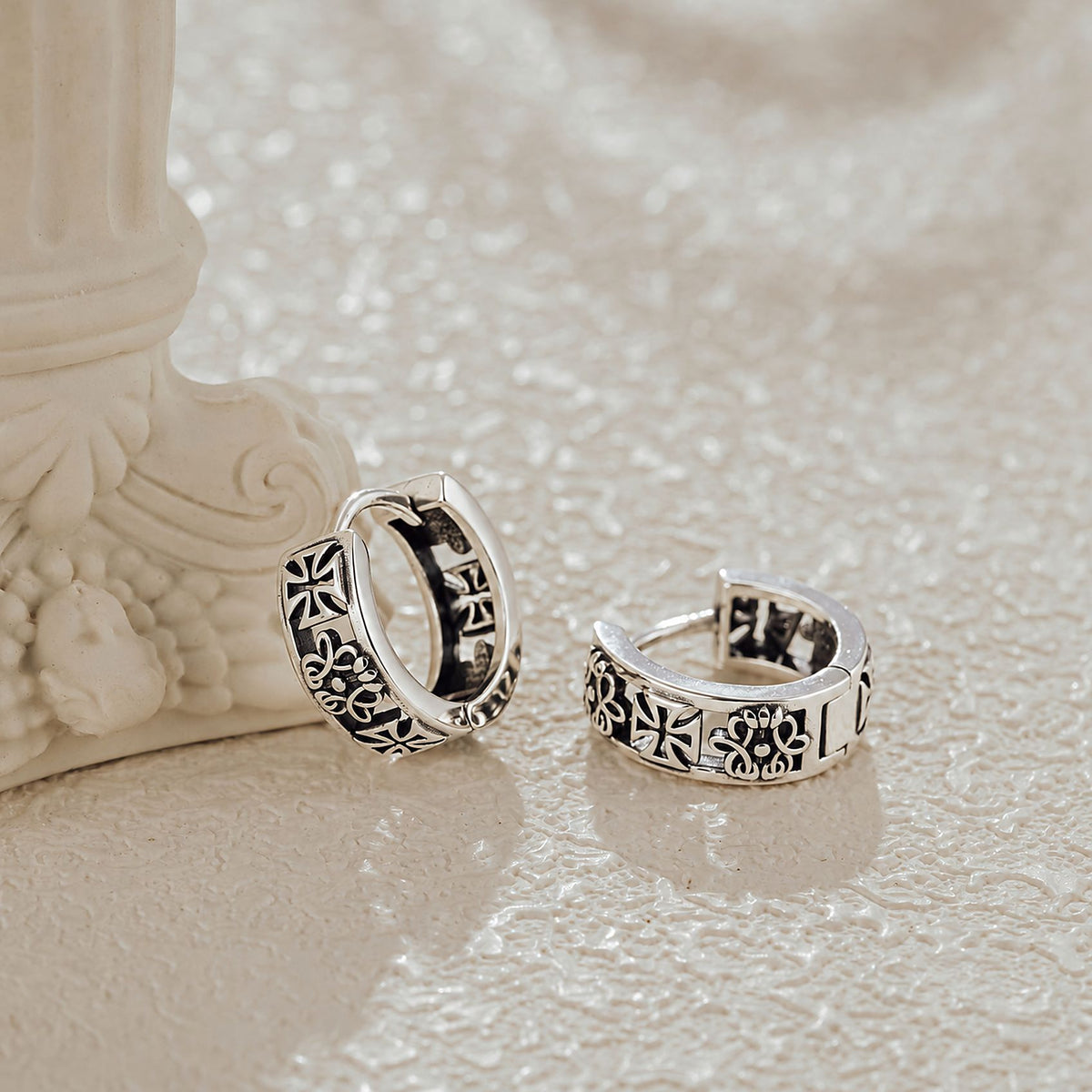 Close-up of oxidized silver gothic huggie showing cross and floral engraving detail