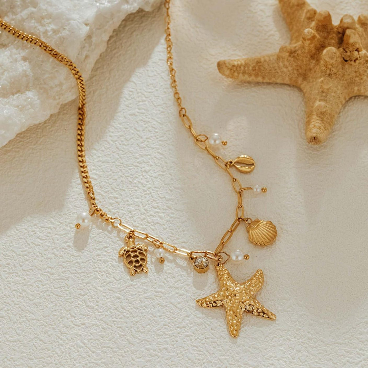 Asymmetric gold chain detail, paperclip links on one side and fine curb links on the other, beside a starfish