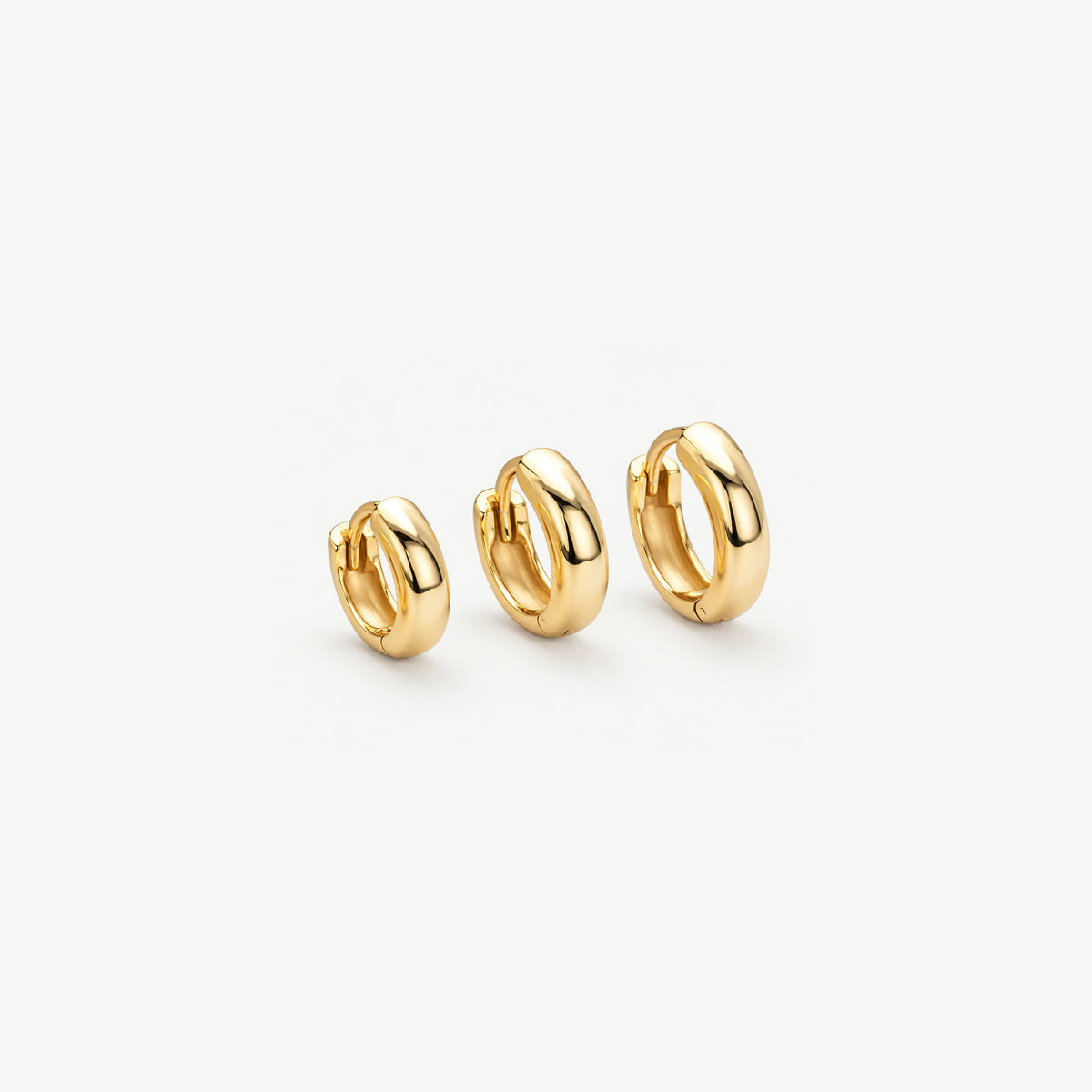 Three polished gold huggie hoops in 7 mm, 8 mm and 9 mm lined up at an angle, showing the dome and the hinge