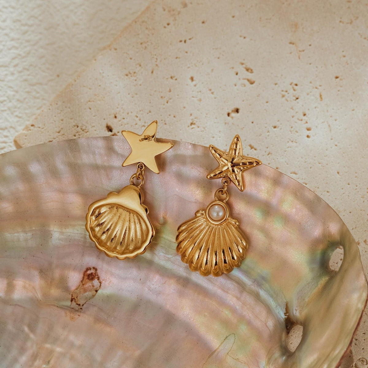 Front and back of the gold seashell drop earrings on mother of pearl, one turned to show the smooth reverse