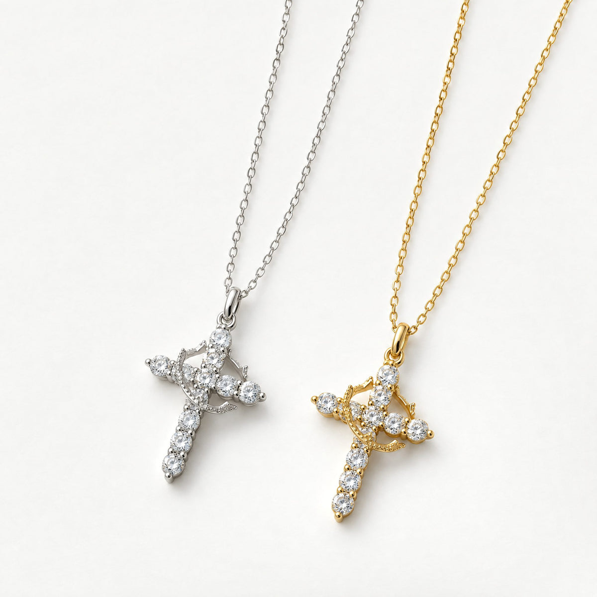 Silver and gold plated crown cross pendant necklaces set with clear cubic zirconia, side by side on off-white