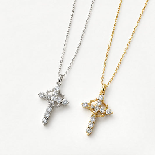 Silver and gold plated crown cross pendant necklaces set with clear cubic zirconia, side by side on off-white