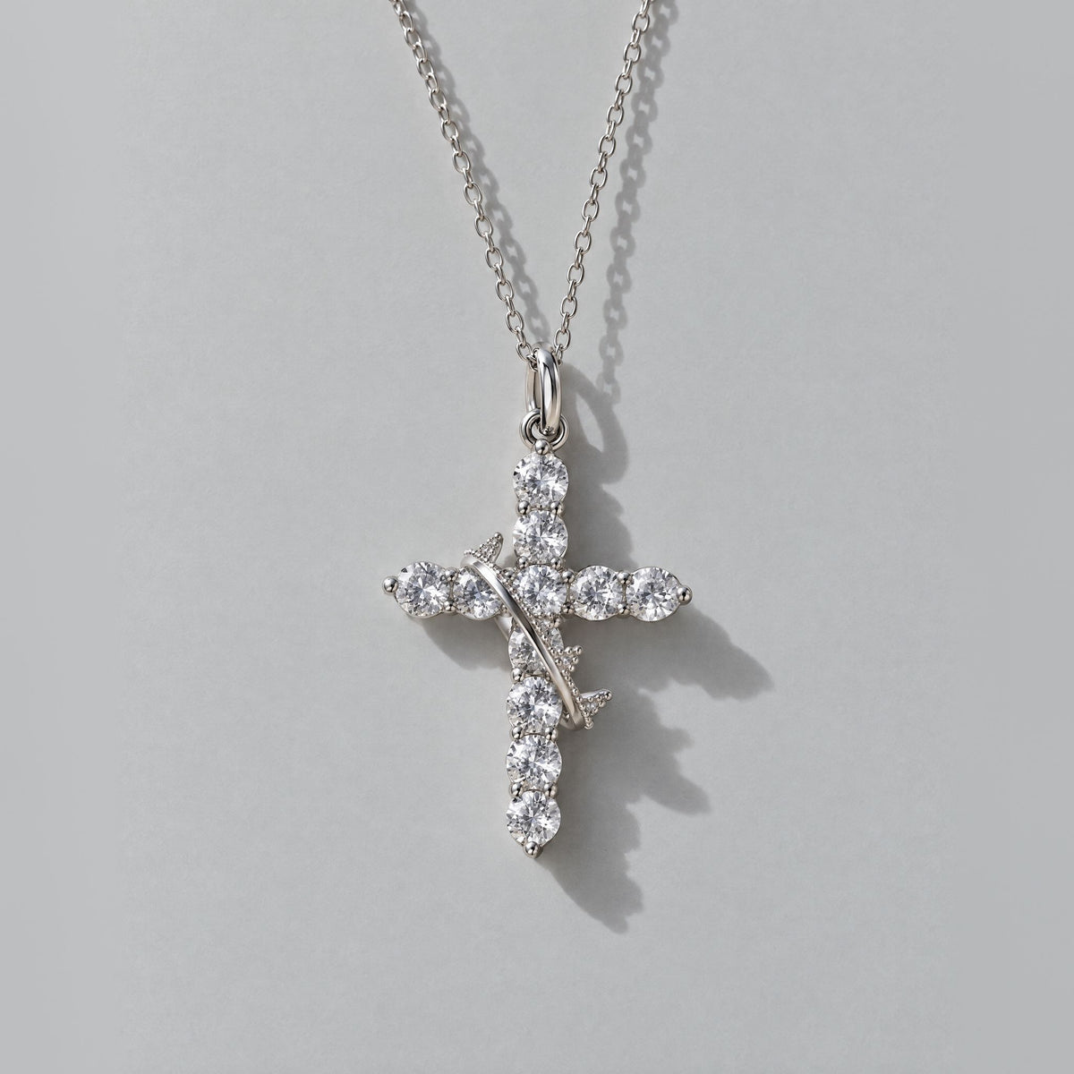 Silver crown cross pendant with clear cubic zirconia and a rotating crown ring, seen from above on dove grey