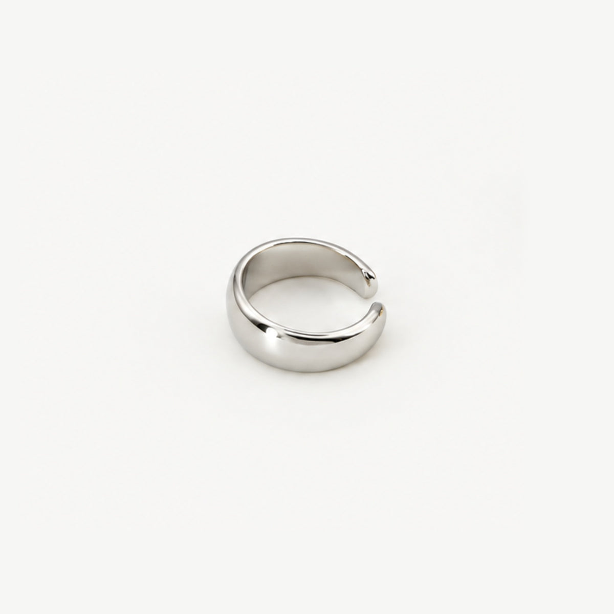 Sterling silver dome ear cuff lying at an angle, rounded high-polish band seen from the outer side