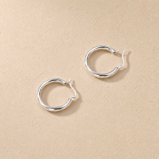 Faceted sterling silver hoop earrings shown open, top-down on warm cream background