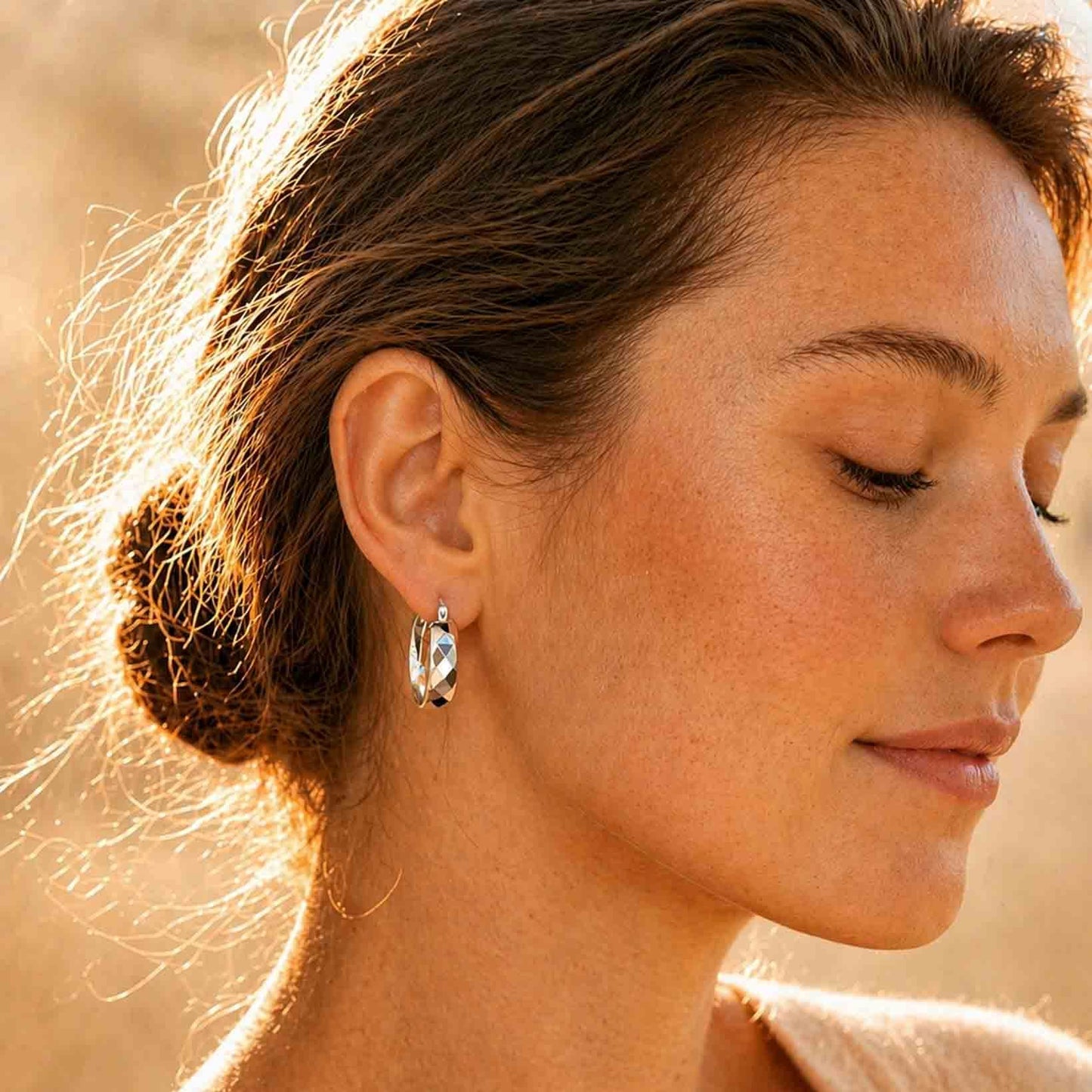 Woman wearing chunky faceted sterling silver hoop earrings, side profile in warm light
