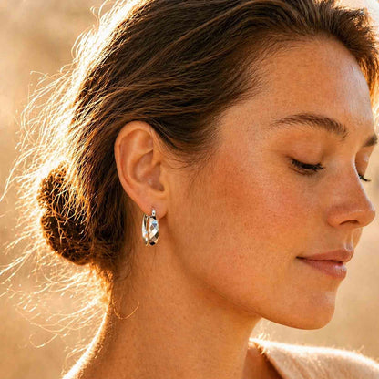 Woman wearing chunky faceted sterling silver hoop earrings, side profile in warm light
