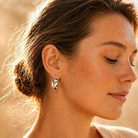 Woman wearing chunky faceted sterling silver hoop earrings, side profile in warm light