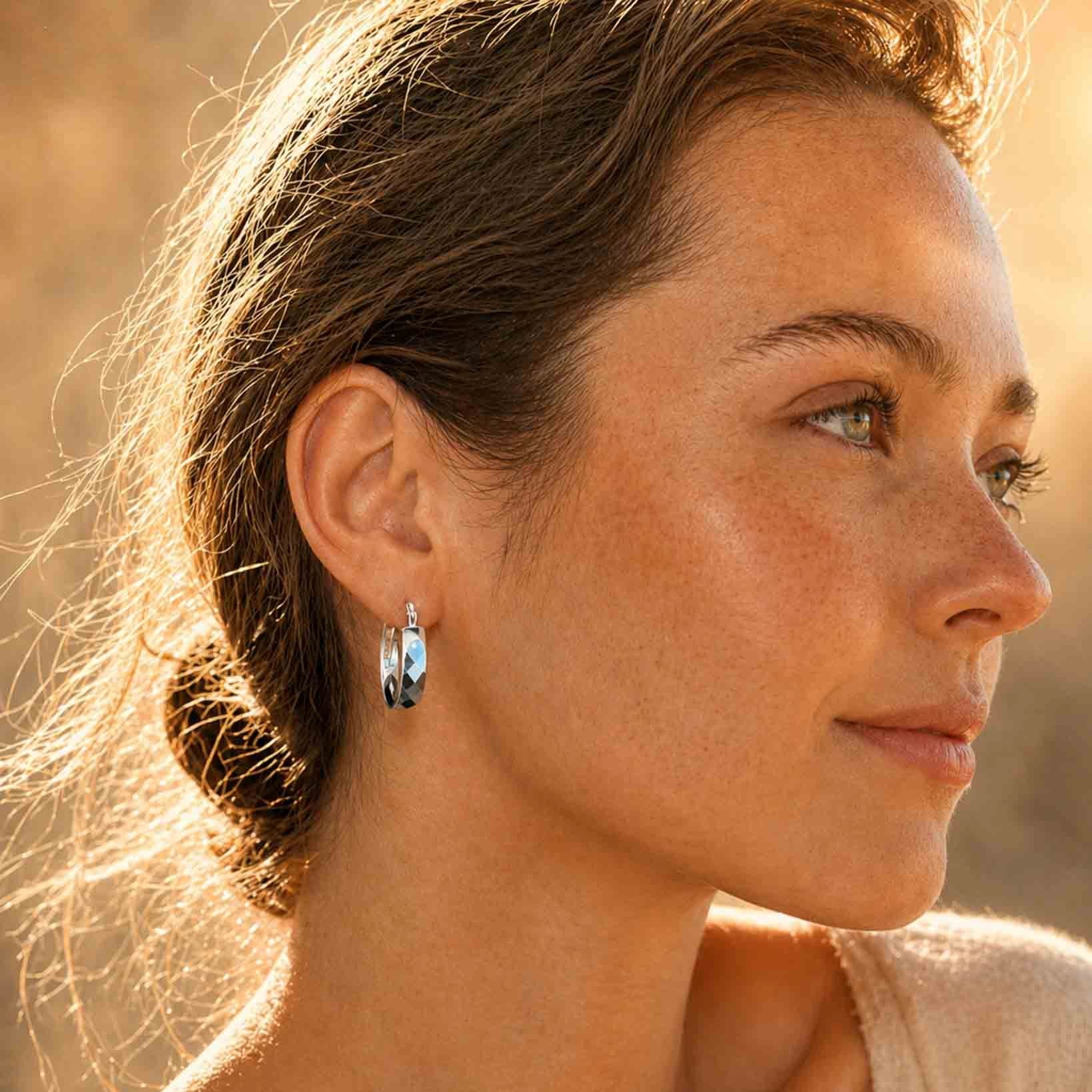 Faceted sterling silver hoop earrings worn on model, side view with hair tied back