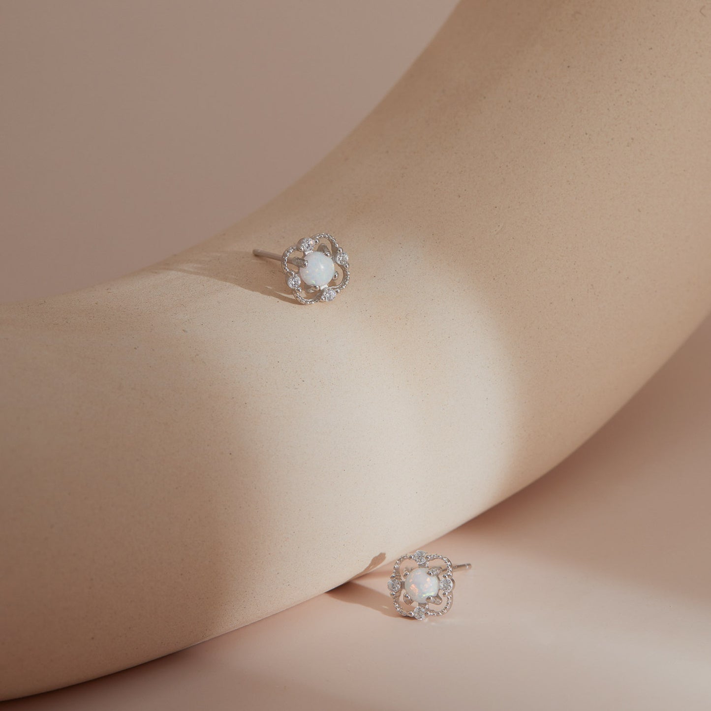 Silver floral opal stud earrings on a smooth sculptural surface