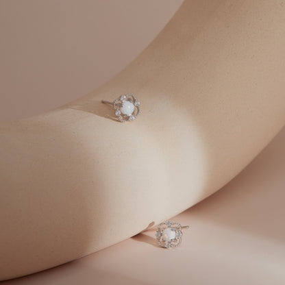 Silver floral opal stud earrings on a smooth sculptural surface