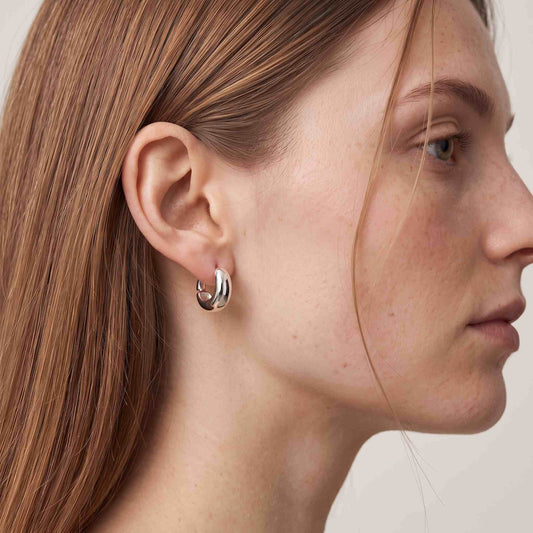 Woman wearing a sterling silver chunky dome huggie hoop earring, side profile view on model