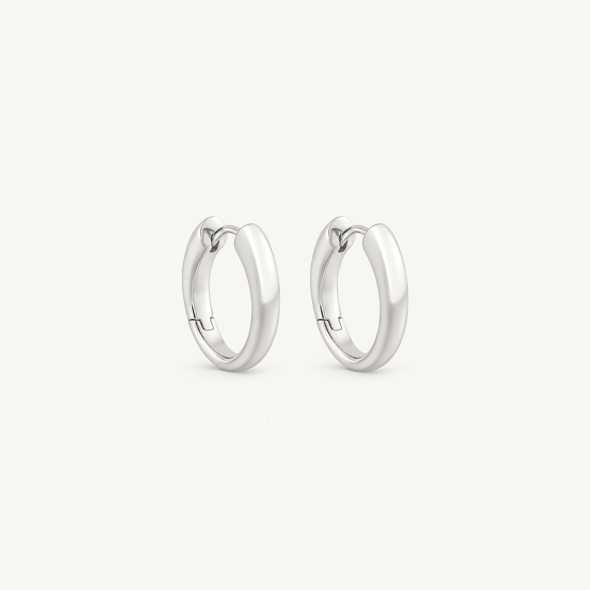 Pair of sterling silver huggie hoops angled to show the tapered band, the clicker wire and the stepped hinge seam