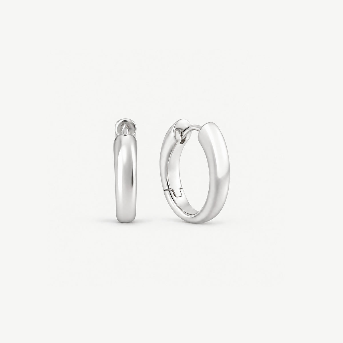 Tapered sterling silver huggie hoop earrings standing upright, a front view beside a three-quarter view of the hinge