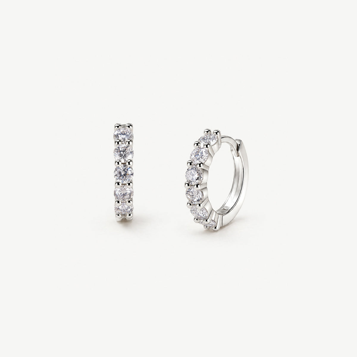 Sterling silver moissanite huggie hoops on off-white, one facing forward with its stone row, one turned to the hinge