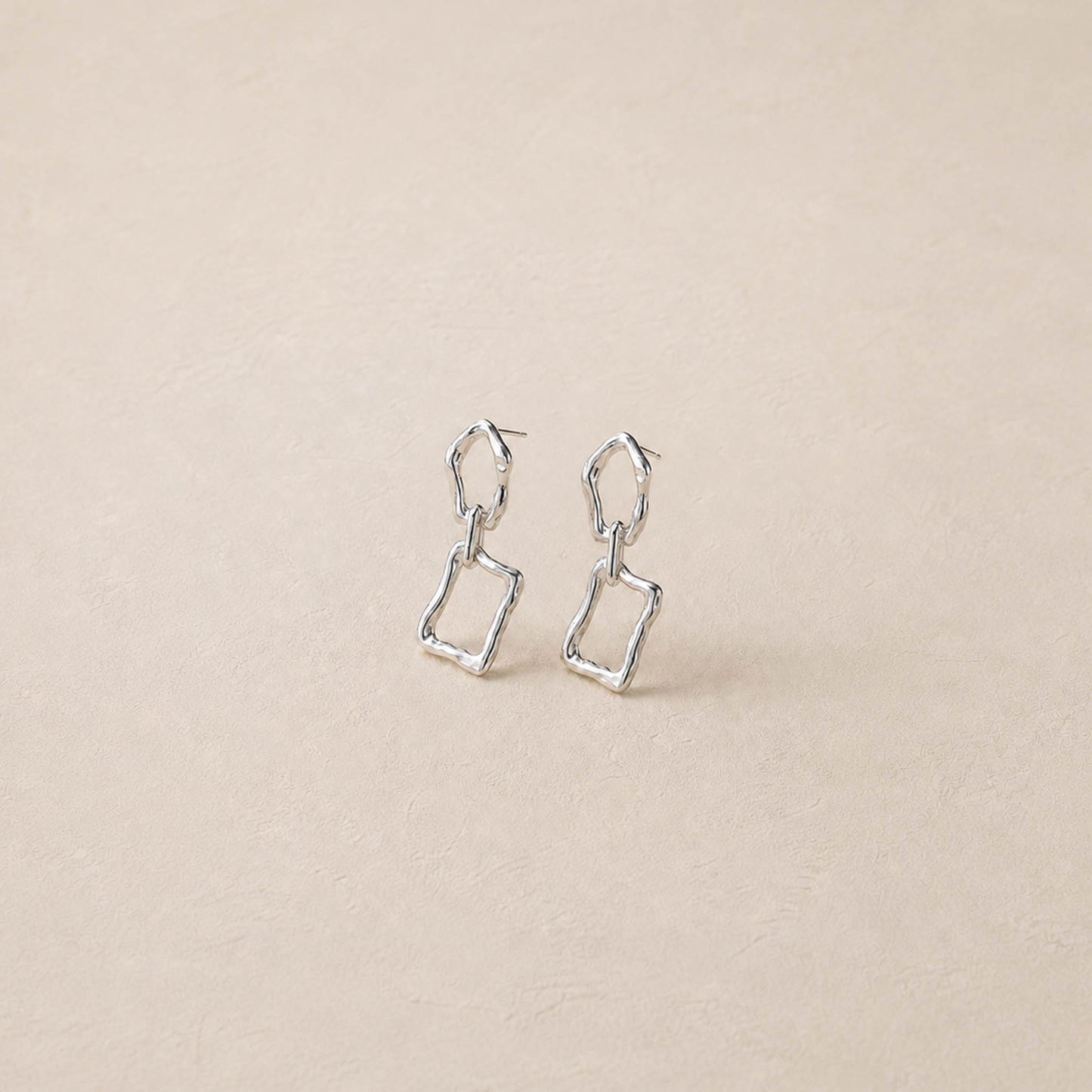 Pair of sterling silver sculptural dangle earrings on cream backdrop, two irregular linked frames per ear