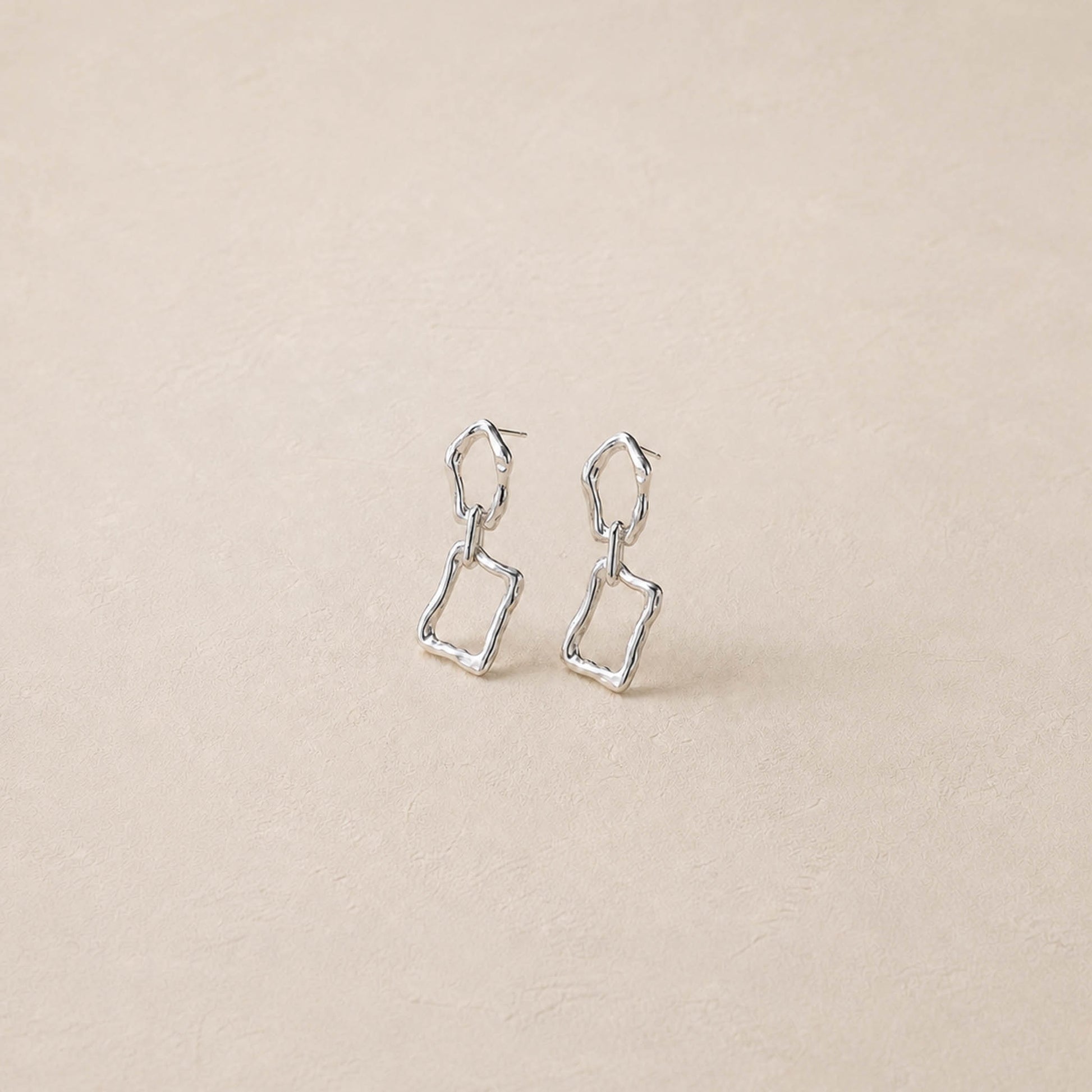 Pair of sterling silver sculptural dangle earrings on cream backdrop, two irregular linked frames per ear