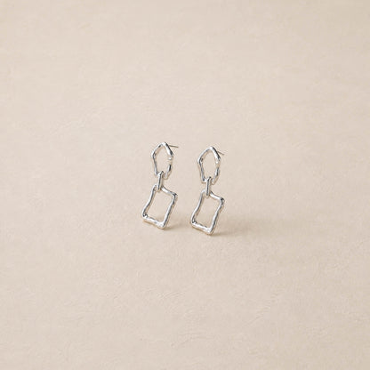 Pair of sterling silver sculptural dangle earrings on cream backdrop, two irregular linked frames per ear
