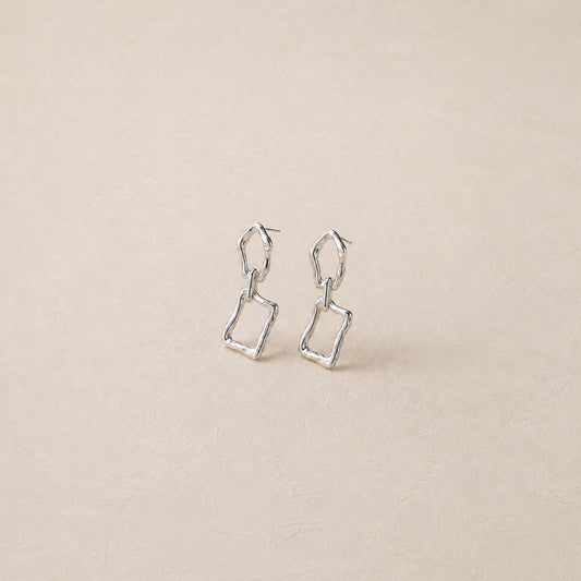 Pair of sterling silver sculptural dangle earrings on cream backdrop, two irregular linked frames per ear