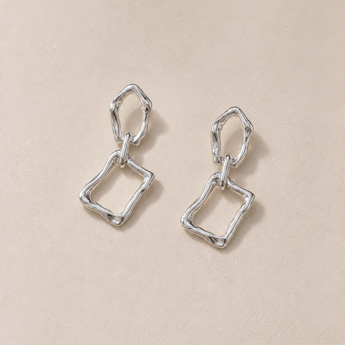 Close-up of sterling silver dangle earrings showing molten pebble top and irregular rectangular frame below