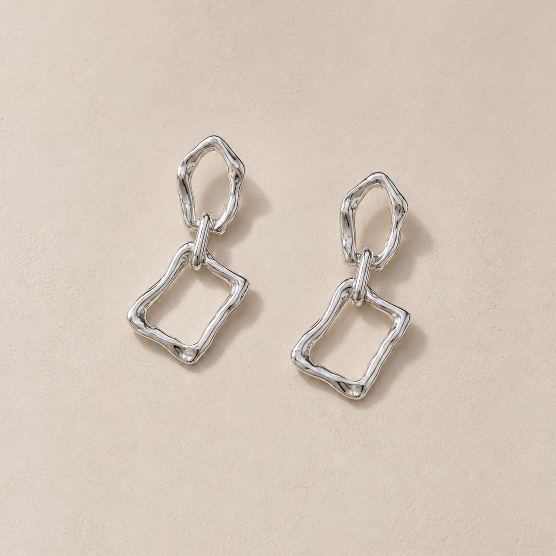 Close-up of sterling silver dangle earrings showing molten pebble top and irregular rectangular frame below