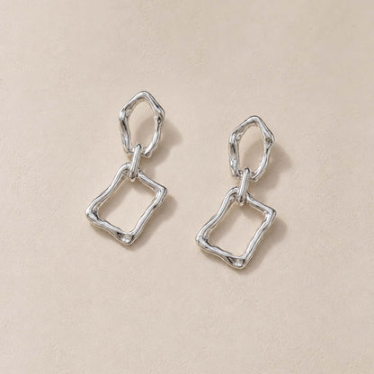 Close-up of sterling silver dangle earrings showing molten pebble top and irregular rectangular frame below