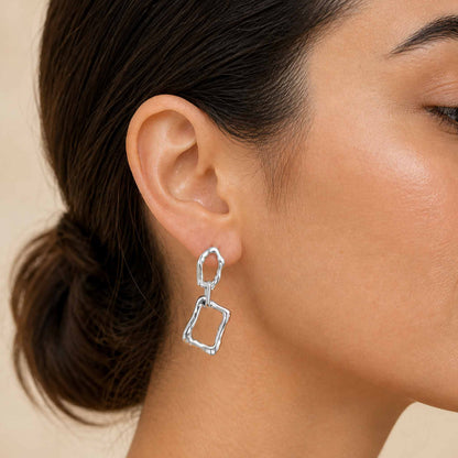 Sterling silver linked-frame dangle earring close-up on dark-haired model's ear, hair pulled back