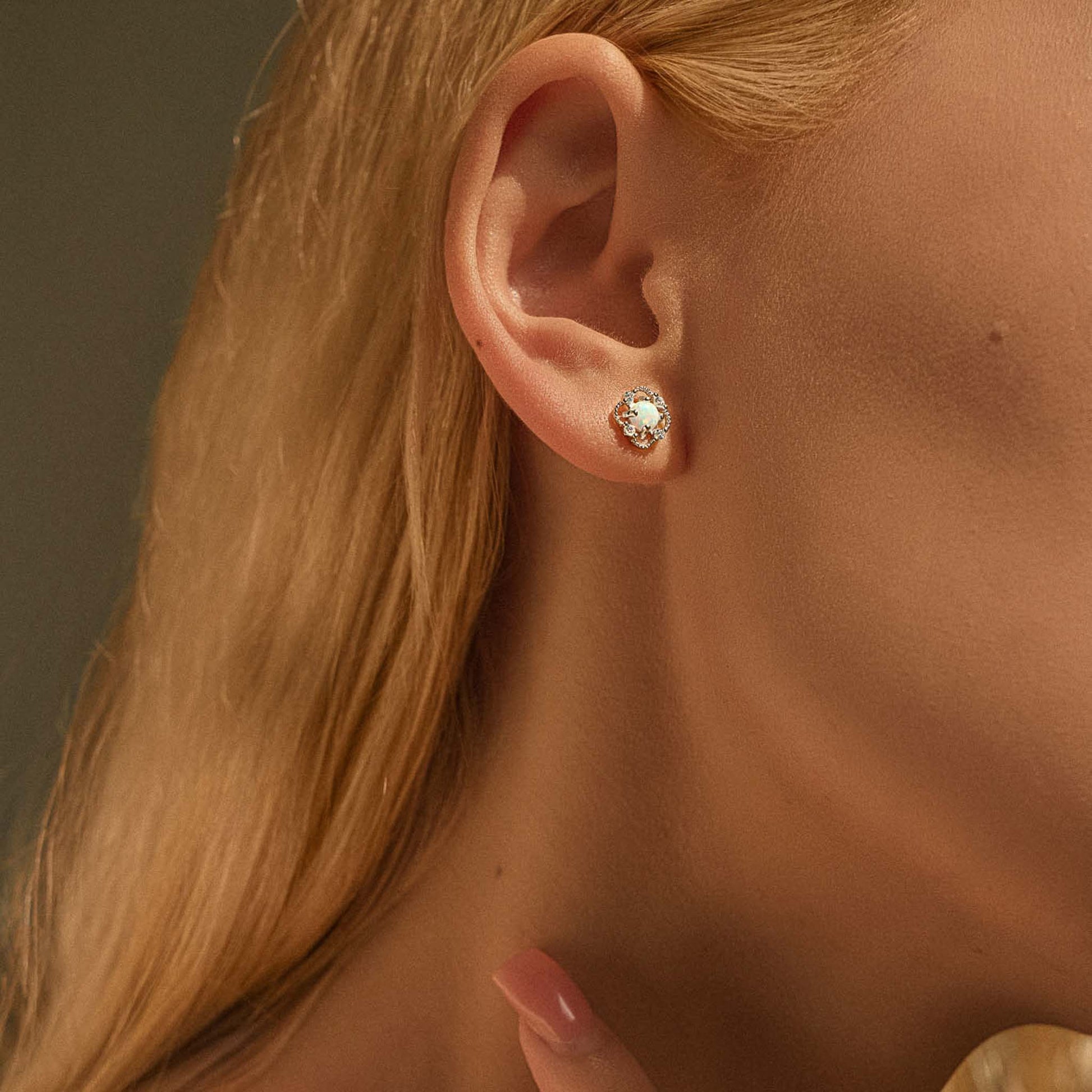 Close-up of silver opal floral stud earring worn on ear for scale.