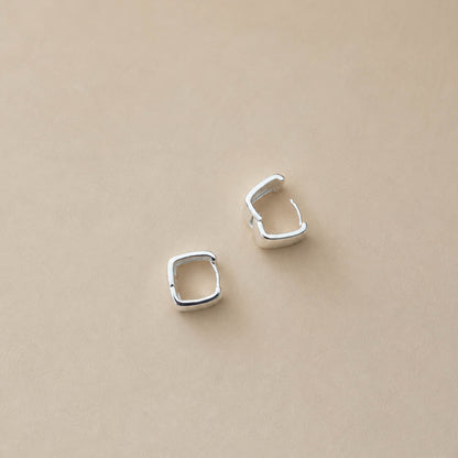 Pair of sterling silver chunky square huggie hoop earrings on cream backdrop, polished mirror finish