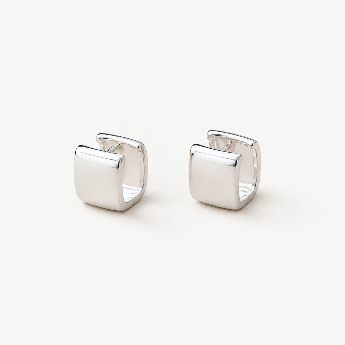 Pair of chunky square sterling silver huggie hoop earrings standing upright, polished finish on near-white background