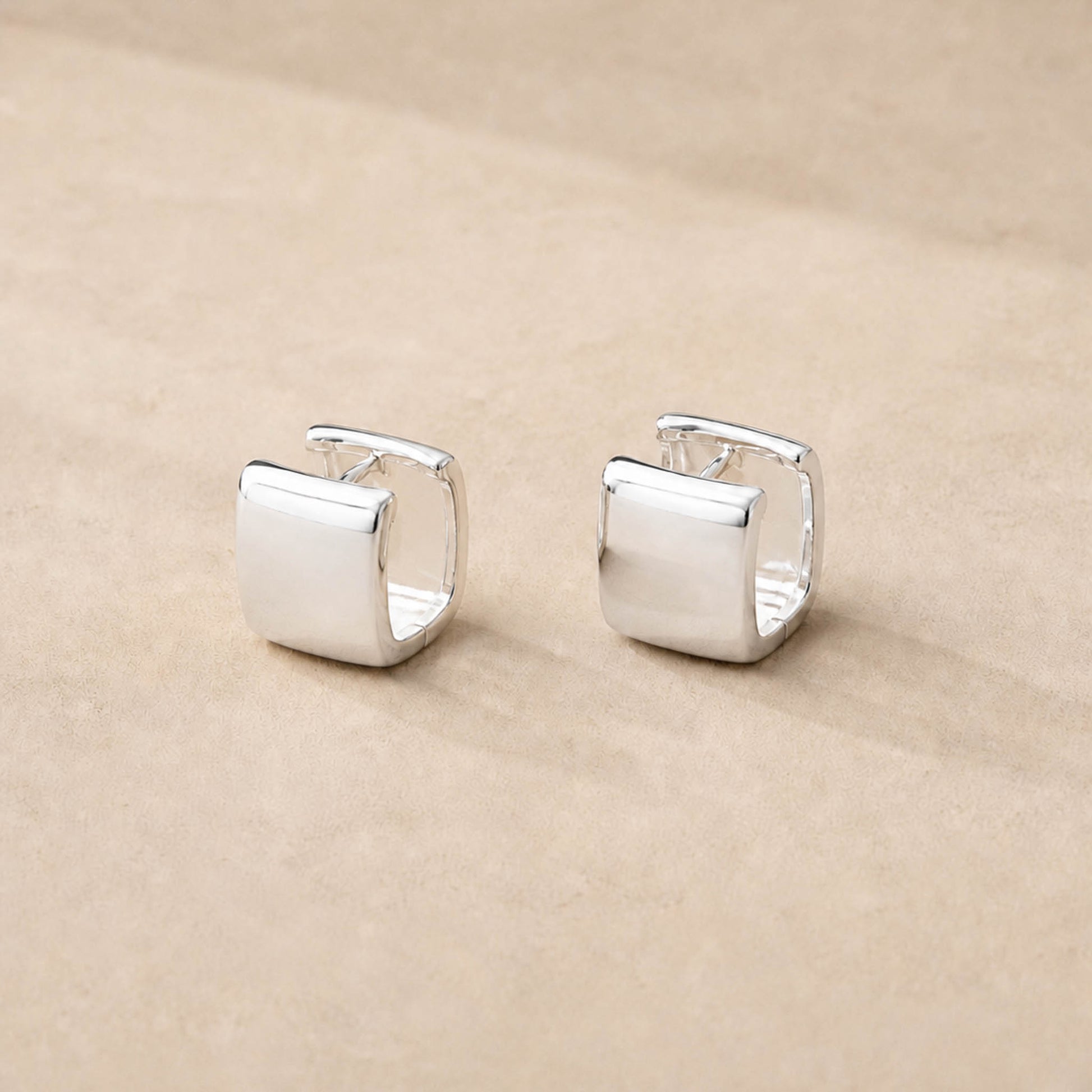 Close-up of sterling silver square huggie hoop earrings showing wide chunky band and high-polish surface