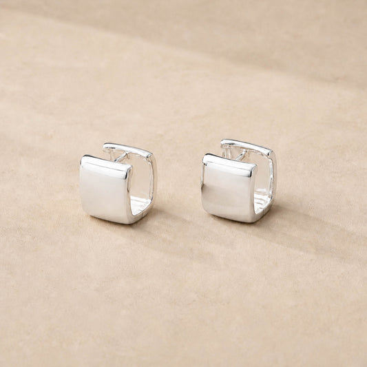 Close-up of sterling silver square huggie hoop earrings showing wide chunky band and high-polish surface