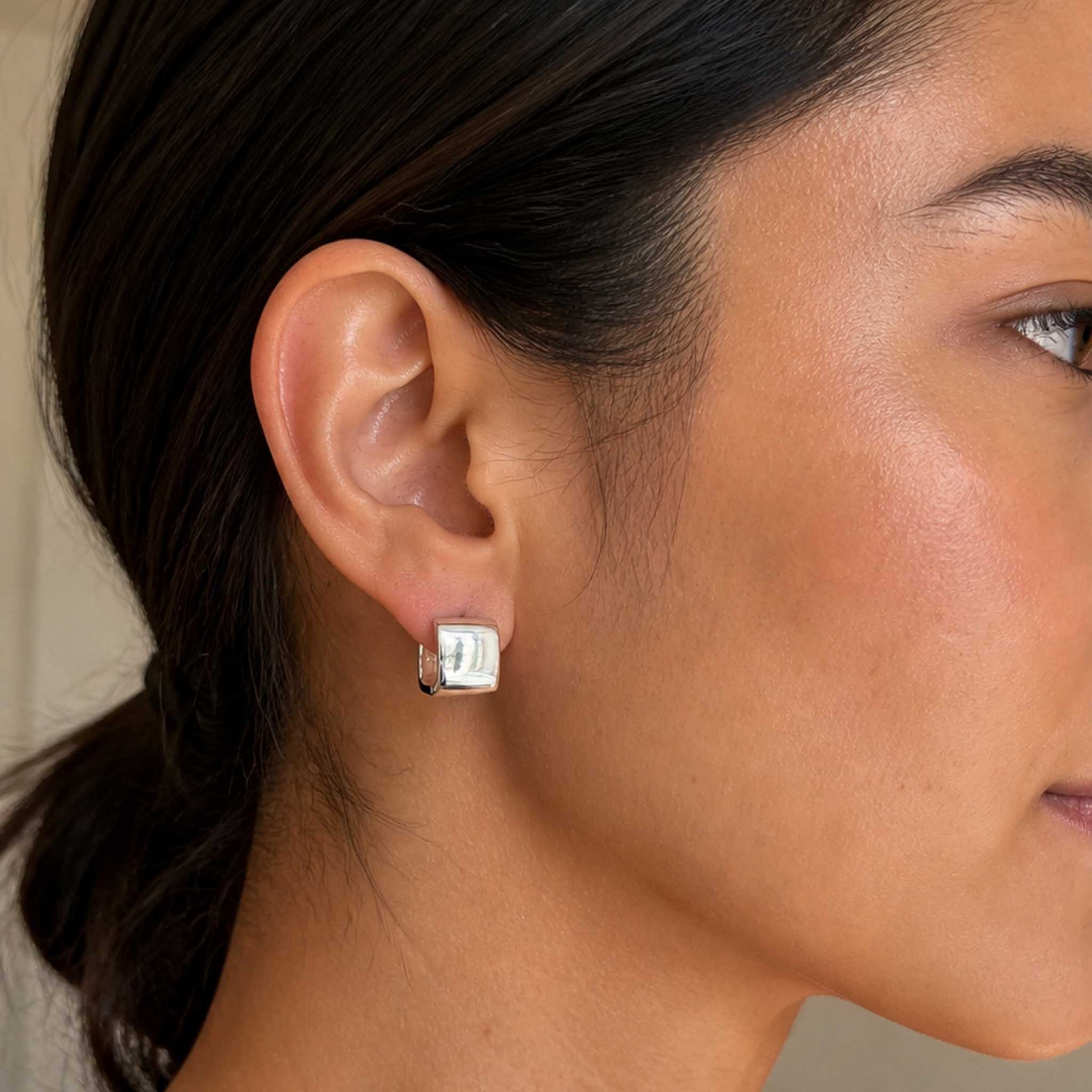 Sterling silver square huggie hoop earring close-up on dark-haired model's ear, low ponytail style