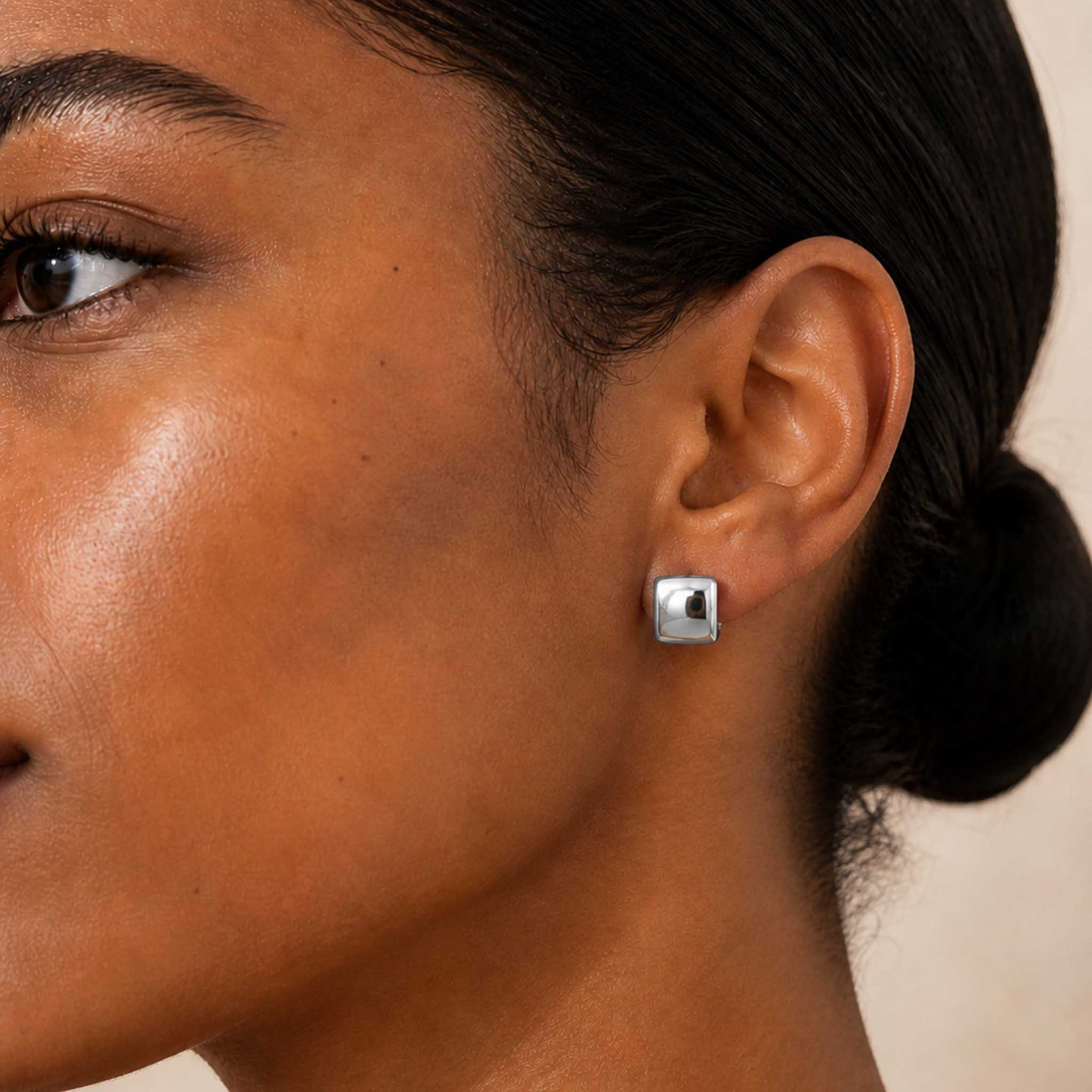 Sterling silver chunky square huggie hoop earring worn on a model's earlobe, shown in side profile.