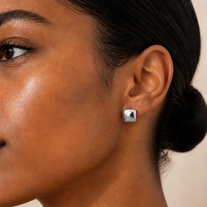 Sterling silver chunky square huggie hoop earring worn on a model's earlobe, shown in side profile.