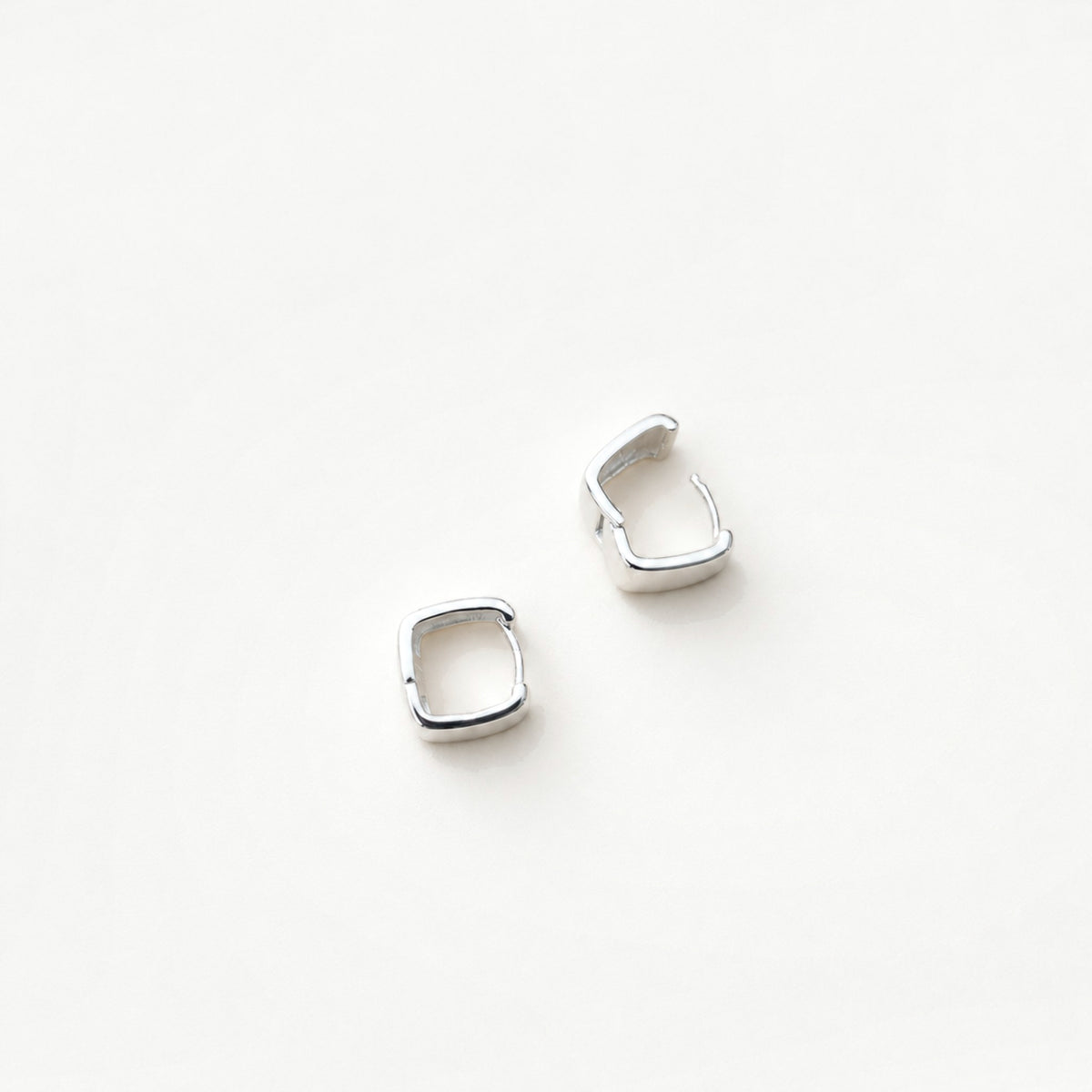 Chunky square sterling silver huggie hoop earrings with hinged closures open, top-down view on near-white background