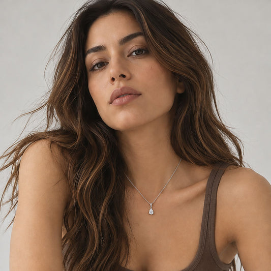 Woman with long wavy brown hair in a brown ribbed tank wearing a dainty silver tone pear pendant necklace