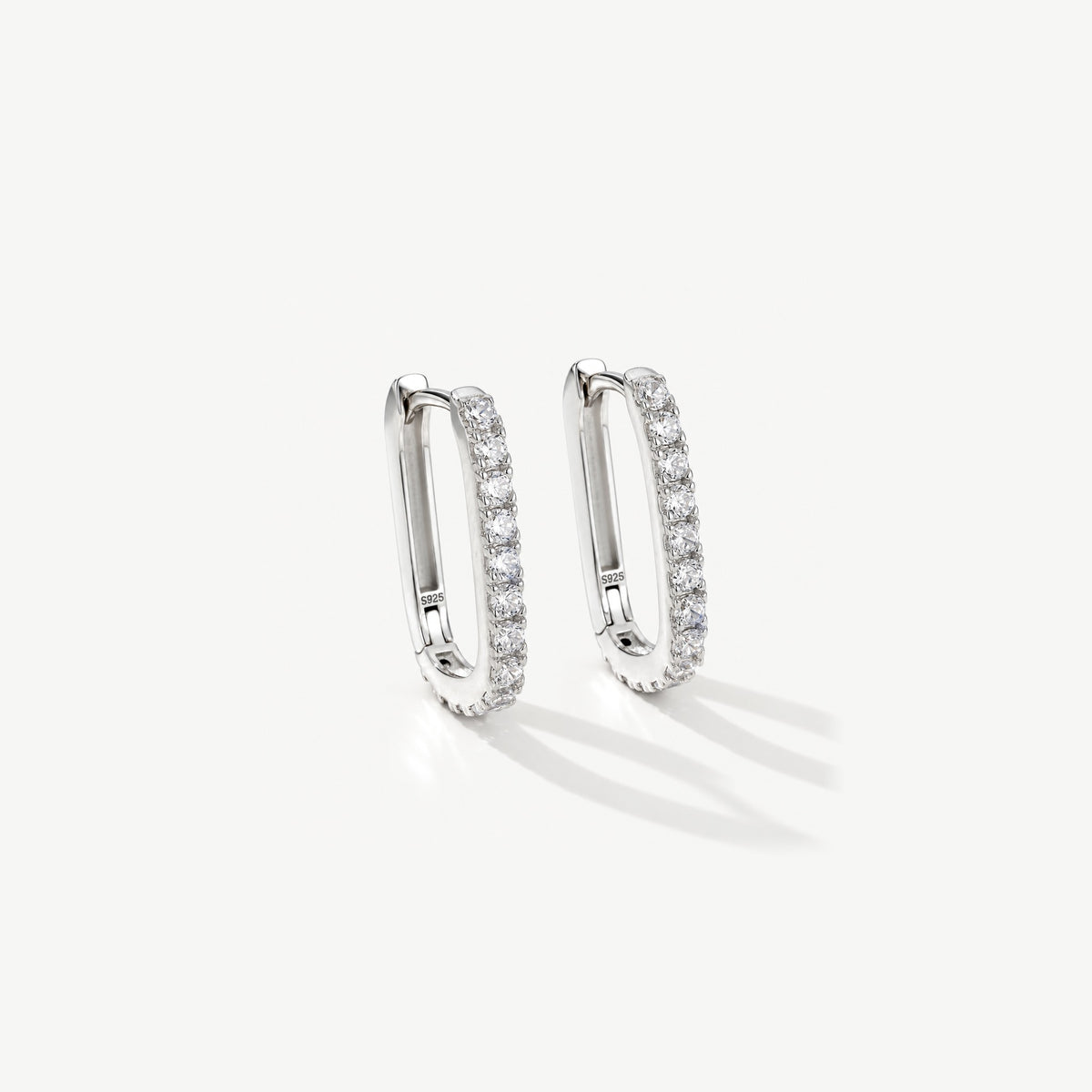 Pair of sterling silver pavé U hoop huggie earrings standing on off-white, the hinge visible on the inner side