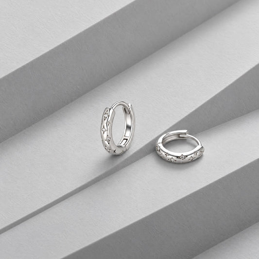 Small sterling silver star huggie hoops on folded grey card, one upright showing the engraved stars, one flat
