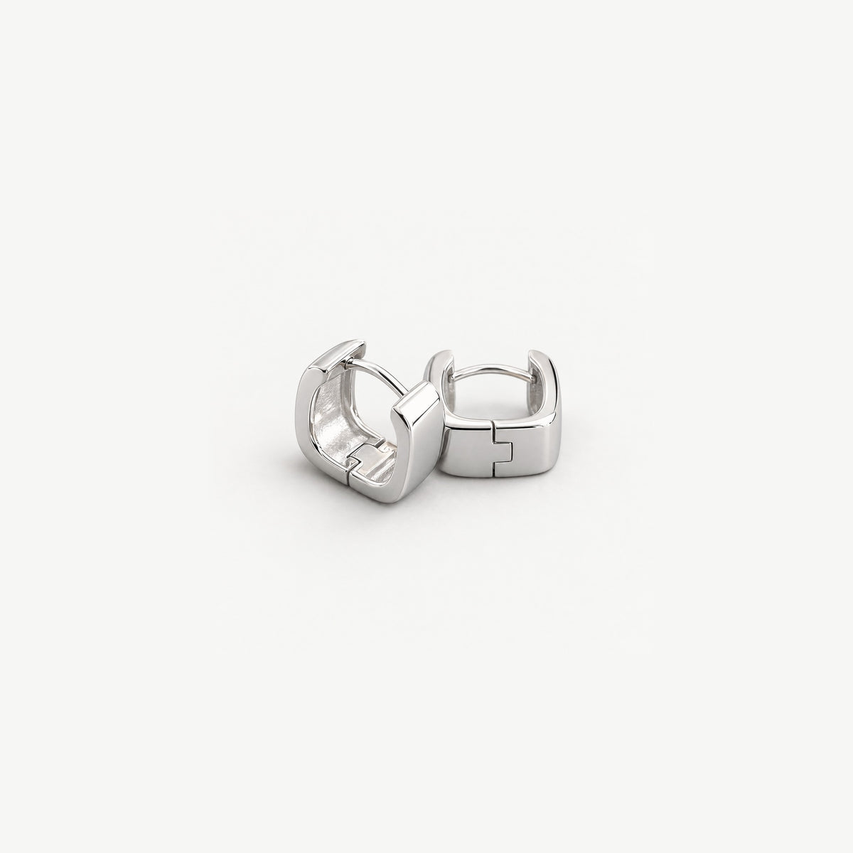 Two square huggie earrings stacked on a diagonal, showing the hinge seam across the wide band and the polished interior