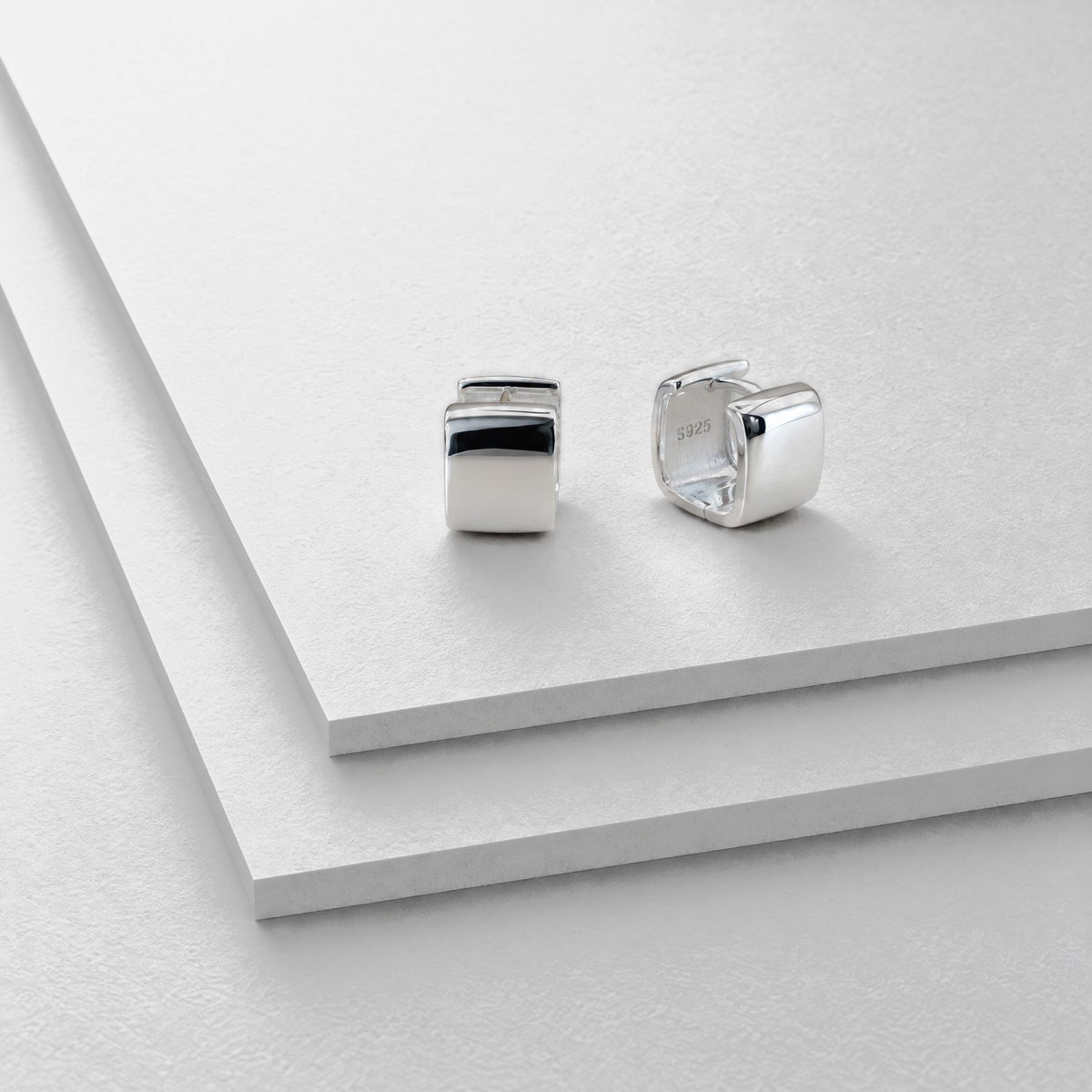 Chunky square sterling silver huggie earrings on stepped grey card, one facing forward, one turned to show the hinge
