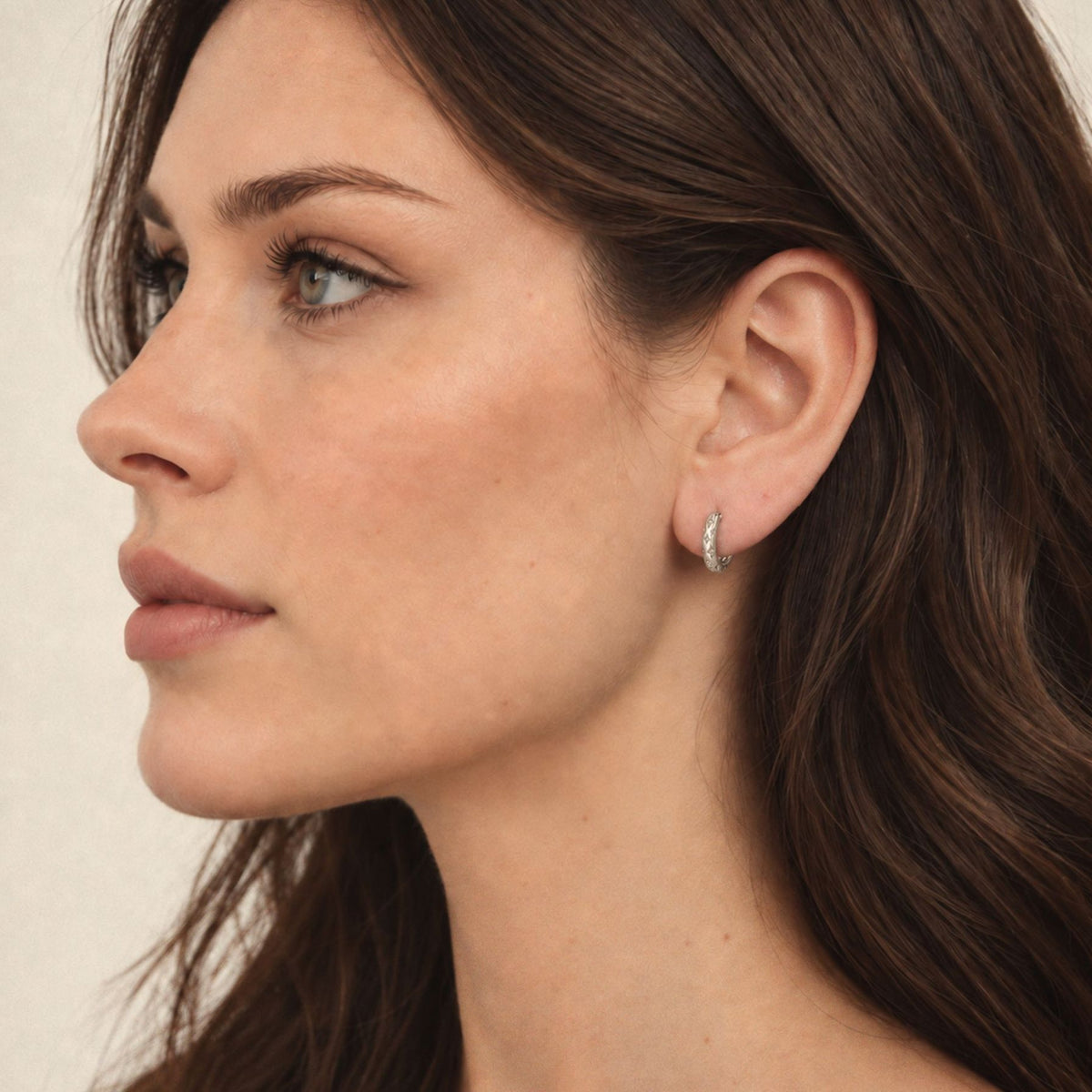 Woman wearing a small sterling silver star huggie hoop earring, side profile showing its size on the ear
